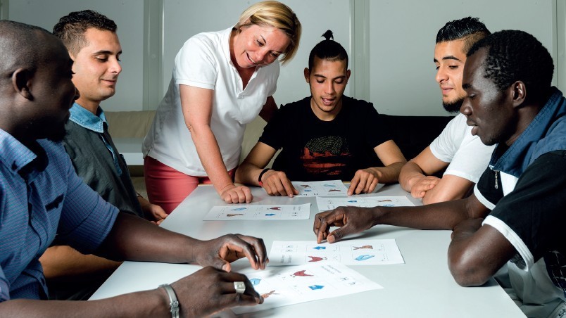 Das Bild zeigt einige jüngere Menschen unterschiedlicher Herkunft, die an einem Seminartisch sitzen und an Dokumenten arbeiten.